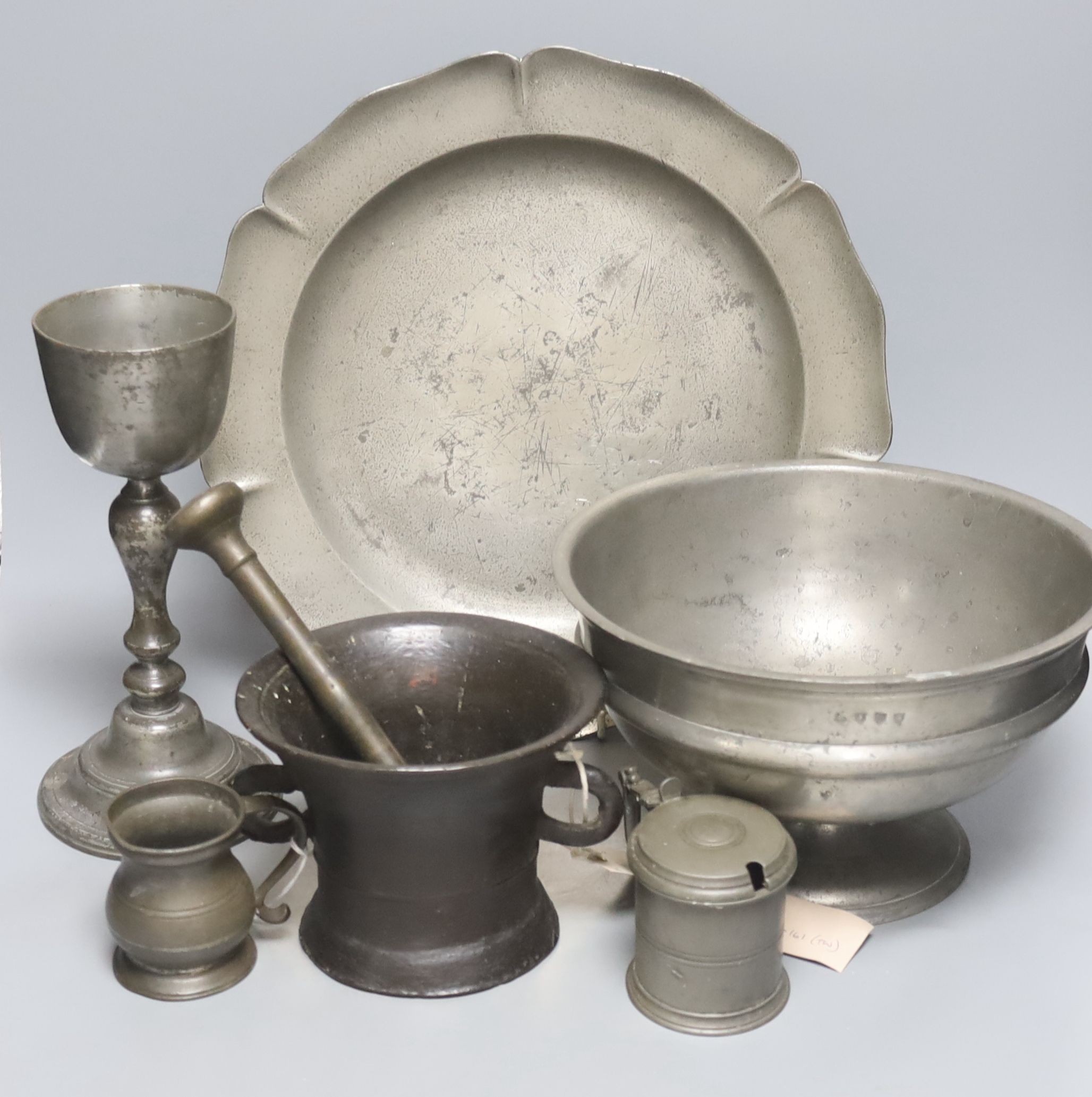 A pewter pedestal bowl, a barbed and crested dish, three other items of pewter and a 17th/18th century bronze pestle and mortar